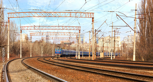 Passenger train cars of the train ride on the railway tracks in the background of the cityscape