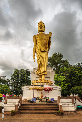 Buddha in the storm. A standing golden buddha statue against a stormy sky near the border point where the Mekong river leaves Thailand to enter Laos -   Phra Yai Phu Khok Ngio 
