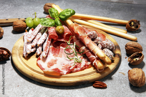 Food tray with delicious salami, ham,  fresh sausages and herbs. Meat platter with selection on rustic background
