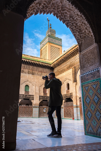 Young European tourist with a camera takes a picture in The Madrasa Bou Inania ( Medersa el Bouanania ) is acknowledged as an excellent example of Marinid architecture. Medina of Fes, Morocco