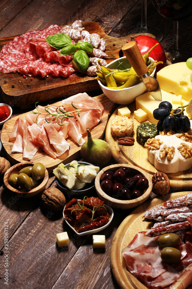 Italian antipasti wine snacks set. Cheese variety, Mediterranean olives, crudo, Prosciutto di Parma, salami and wine in glasses over grunge background. Italian antipasti wine snacks set. Cheese variety, Mediterranean olives, crudo, Prosciutto di Parma, salami and wine in glasses over grunge background.