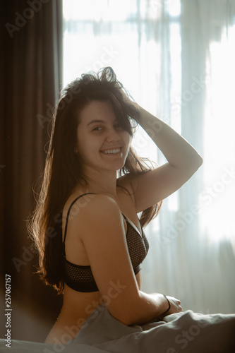 young pretty woman in black bra sitting on bed. morning time