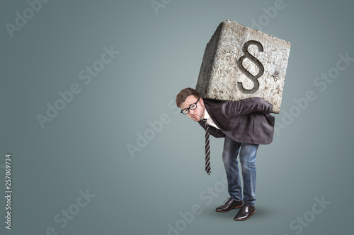 Mann trägt einen schweren Stein mit Paragraph-Symbol auf dem Rücken photo