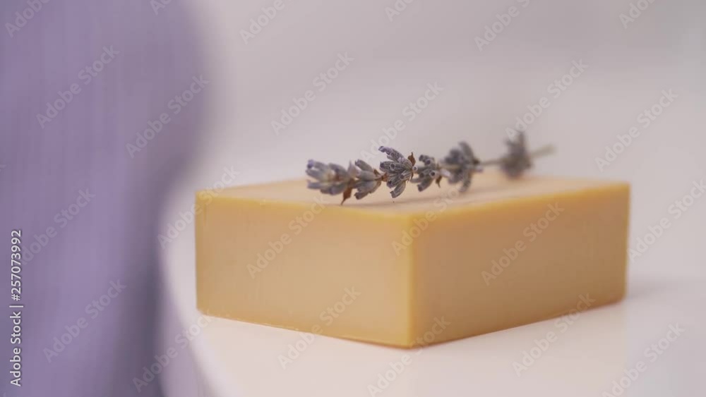 A demonstration close-up video of woman's hand putting a lavender inflorescences on the piece of handmade soap