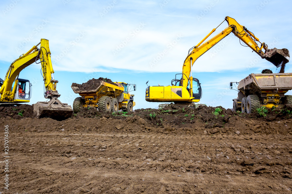 Big excavators are loading two trucks with ground on building site