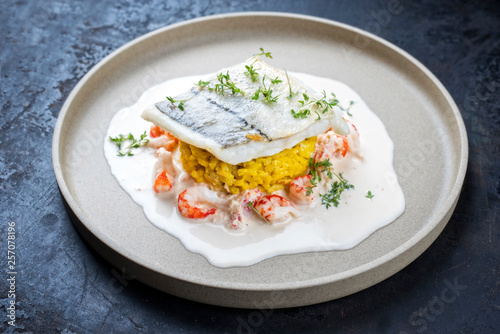 Fried haddock filet with saffron rice and shell prawns in crab sauce as closeup on a modern design plate