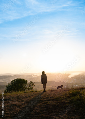 Silhouettes of adorable woman playing running with her cute dog during sunset © alex_marina
