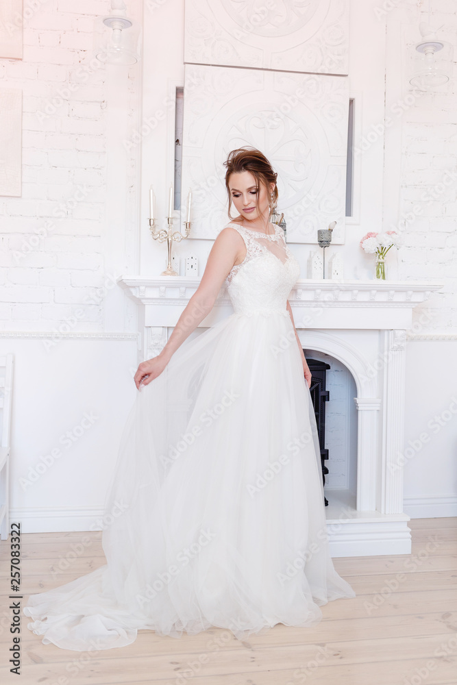 the bride poses near the fireplace in a bright room the bride poses near the fireplace in a bright room