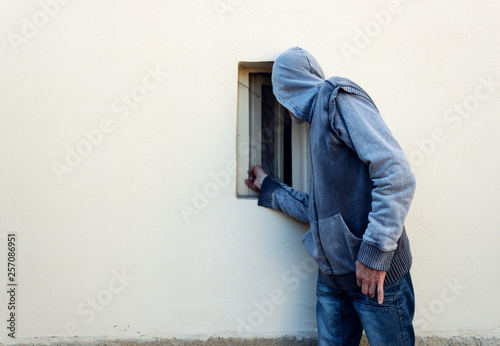 Burglar or thief or robber is looking through the small window and with plan to steal something