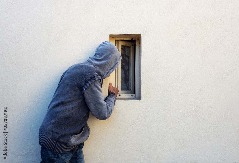 Burglar or thief or robber is looking through the small window and with plan to steal something Burglar or thief or robber is looking through the small window and with plan to steal something