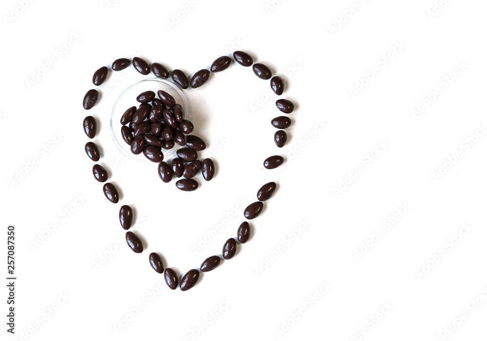 Nuts arranged in heart shape on background. Food image close up candy, chocolate milk, extra dark almond nuts. Love Texture on white grey table top view