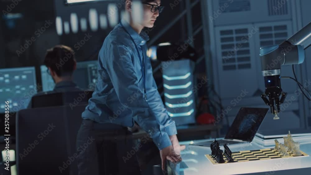Professional Japanese Development Engineer is Testing an Artificial Intelligence Interface by Playing Chess with a Futuristic Robotic Arm. They are in a High Tech Modern Research Laboratory. Professional Japanese Development Engineer is Testing an Artificial Intelligence Interface by Playing Chess with a Futuristic Robotic Arm. They are in a High Tech Modern Research Laboratory.