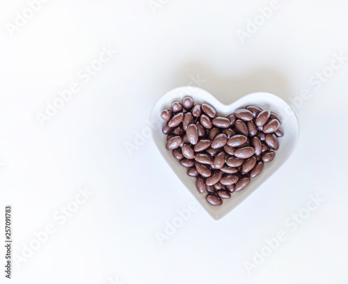 Nuts arranged in heart shape on background. Food image close up candy, chocolate milk, extra dark almond nuts. Love Texture on white grey table top view