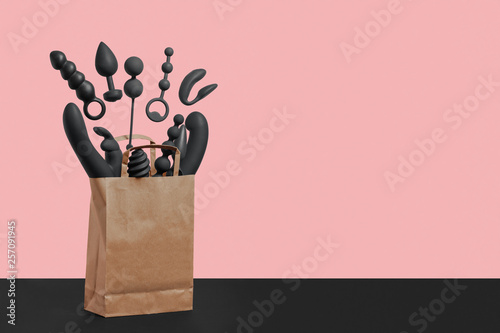 A paper shopping bag filled with black silicone sex toys on a pink background. Erotic toy for fun. Sex gadget and masturbation device. View from above. Place for text. Flat lay. Sex shop concept. photo