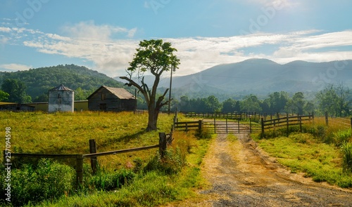 scenic Farm land with tree, wood fence, barn, silo, grass, mountains
