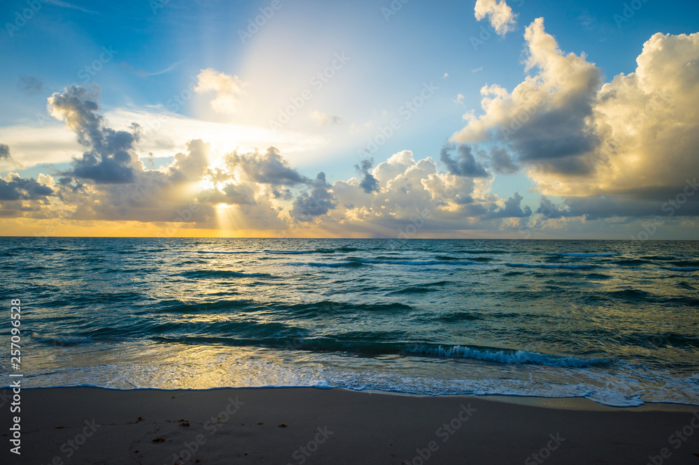 Bright scenic golden sunrise lighting up tropical clouds above gentle waves coming ashore