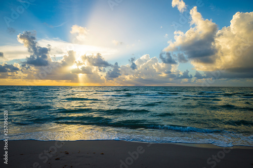 Bright scenic golden sunrise lighting up tropical clouds above gentle waves coming ashore