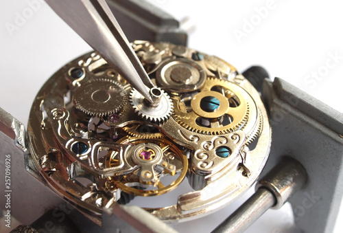 close up of watchmaker repairing old mechanical watch caliber taking small gear with tweezers