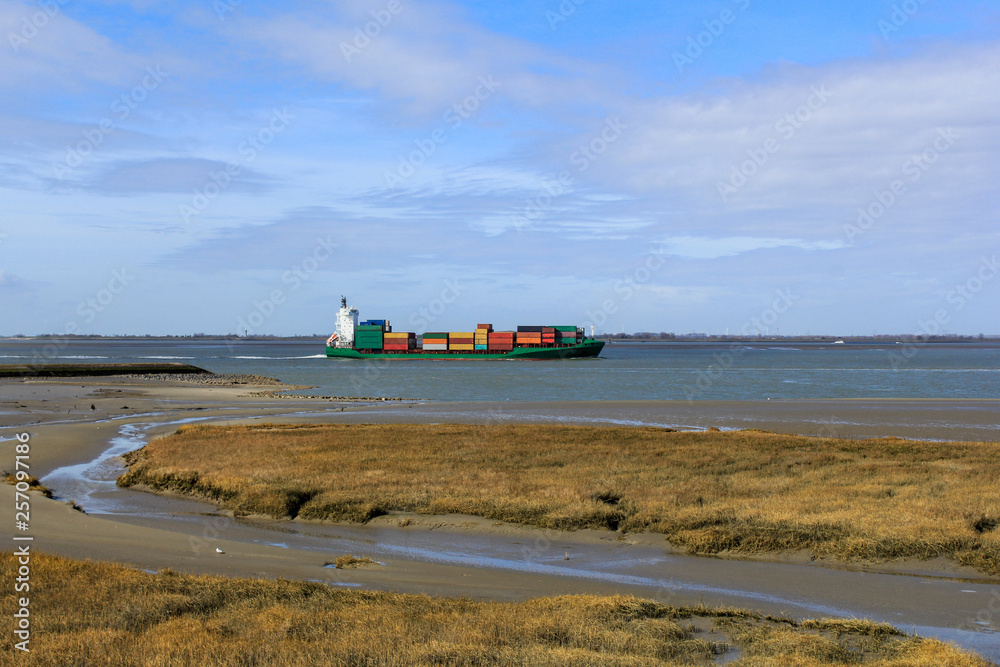 Fototapeta premium a ship sails along the salt marsh towards antwerp in springtime with a blue sky