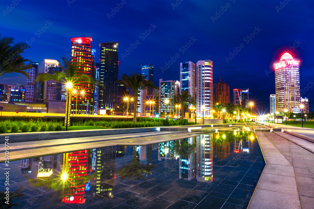 Doha West Bay high rises at night reflecting in the water of downtown park. Lighting skyscrapers of Doha skyline in Qatar, Middle East, Arabian Peninsula in Persian Gulf. Night urban scene.