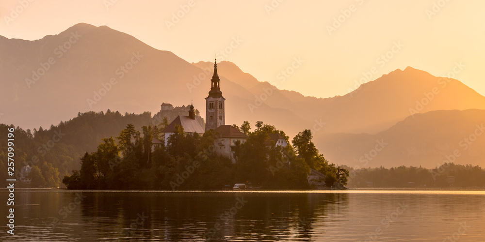 Island with church in lake Bled on orange hazy morning