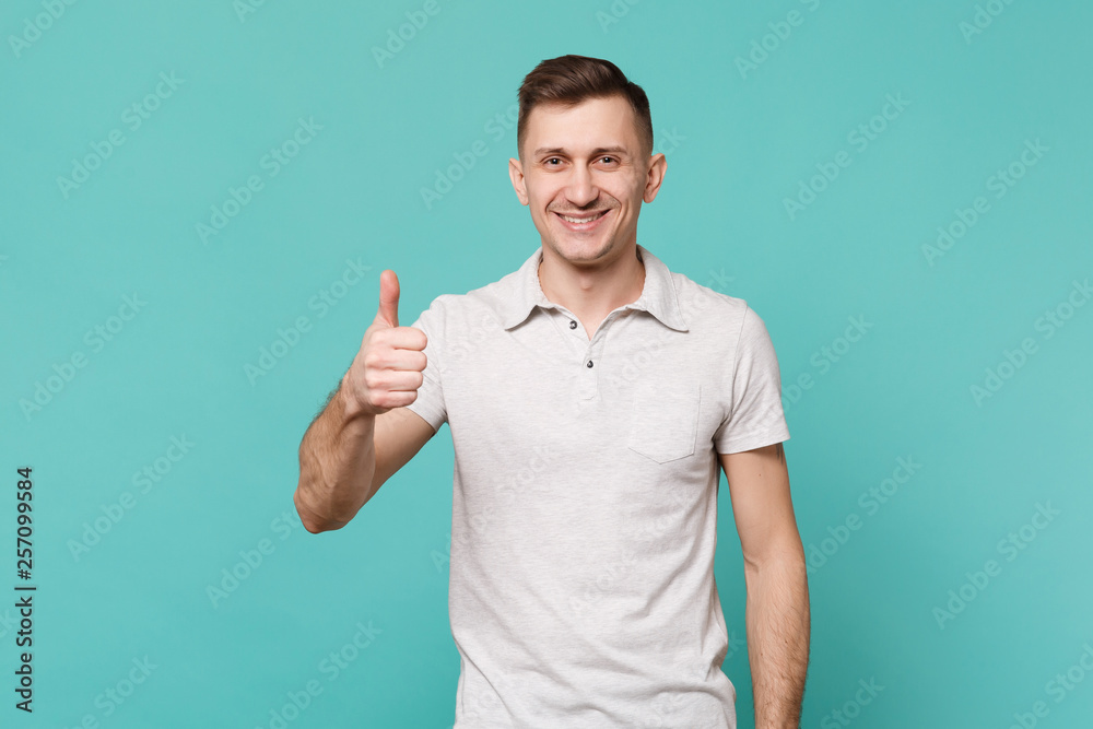 Portrait of smiling handsome young man in casual clothes standing showing thumb up isolated on blue turquoise wall background in studio. People sincere emotions, lifestyle concept. Mock up copy space. Portrait of smiling handsome young man in casual clothes standing showing thumb up isolated on blue turquoise wall background in studio. People sincere emotions, lifestyle concept. Mock up copy space.