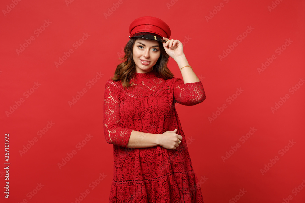 Portrait of beautiful young woman in lace dress holding cap, looking camera, standing isolated on bright red wall background in studio. People sincere emotions, lifestyle concept. Mock up copy space. Portrait of beautiful young woman in lace dress holding cap, looking camera, standing isolated on bright red wall background in studio. People sincere emotions, lifestyle concept. Mock up copy space.