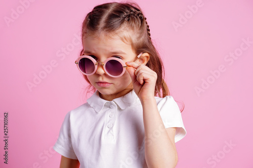 Portrait of beautiful smiling cute model in trendy round sunglasses. Casual 7 y.o. girl posing isolated on pink background. © zamuruev