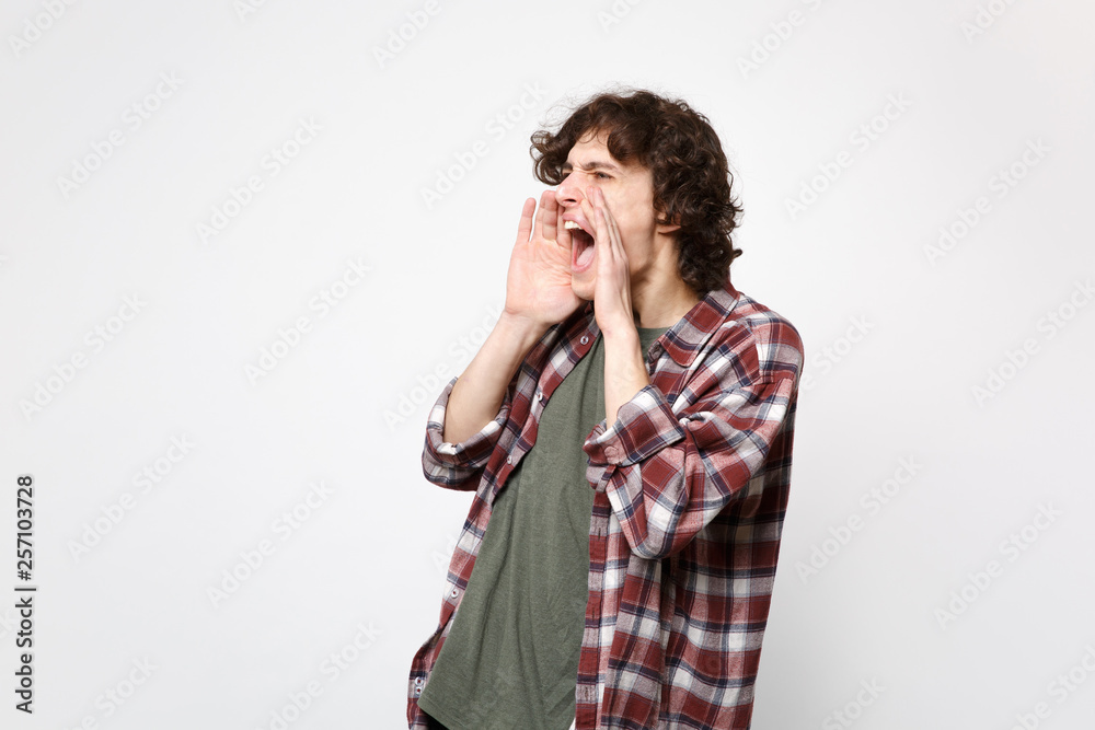 Portrait of young man in casual clothes looking aside screaming with hand gesture near mouth isolated on white wall background in studio. People sincere emotions lifestyle concept. Mock up copy space. Portrait of young man in casual clothes looking aside screaming with hand gesture near mouth isolated on white wall background in studio. People sincere emotions lifestyle concept. Mock up copy space.