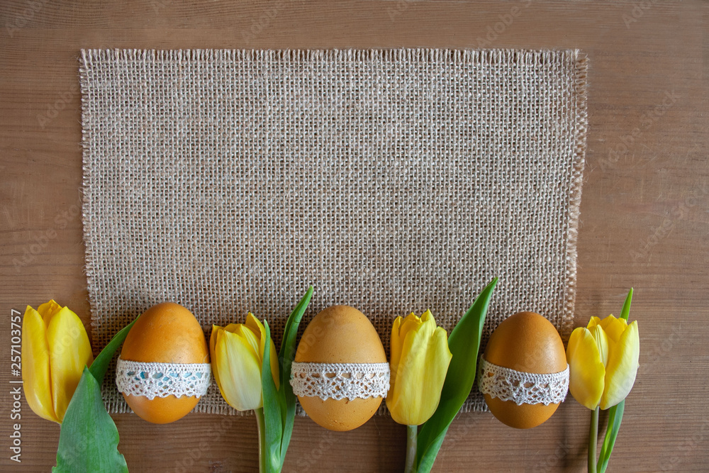 Wielkanocne tło - żółte pisanki i żółte tulipany na tkaninie z juty - obrazy, fototapety, plakaty 