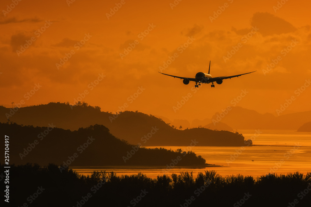 Silhouette plane landing over island and sea