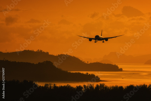 Silhouette plane landing over island and sea