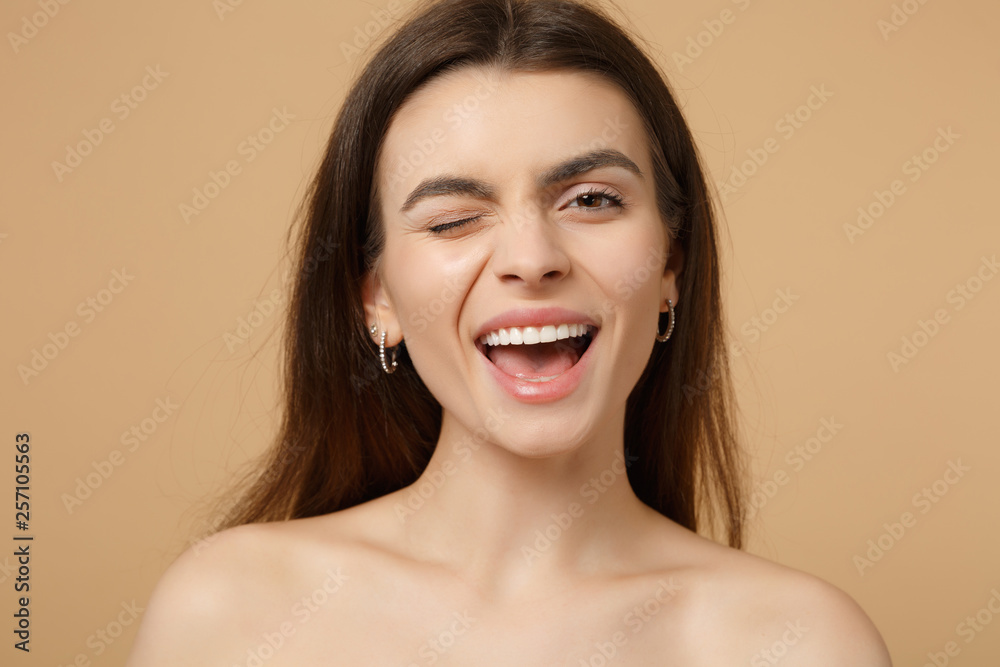 Close up winking smiling brunette half naked woman 20s with perfect skin isolated on beige pastel wall background studio portrait. Skin care healthcare cosmetic procedures concept. Mock up copy space. Close up winking smiling brunette half naked woman 20s with perfect skin isolated on beige pastel wall background studio portrait. Skin care healthcare cosmetic procedures concept. Mock up copy space.