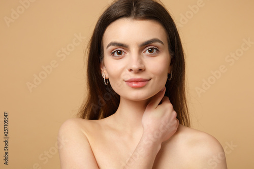 Close up brunette half naked woman 20s with perfect skin, hand on neck isolated on beige pastel wall background, studio portrait. Skin care healthcare cosmetic procedures concept. Mock up copy space.