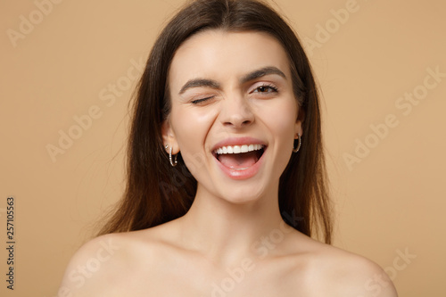 Close up winking smiling brunette half naked woman 20s with perfect skin isolated on beige pastel wall background studio portrait. Skin care healthcare cosmetic procedures concept. Mock up copy space.