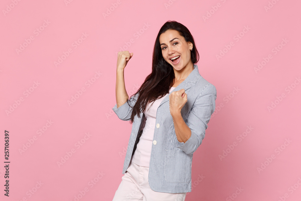 Portrait of joyful happy young woman in striped jacket clenching fists like winner isolated on pink pastel wall background in studio. People sincere emotions, lifestyle concept. Mock up copy space. Portrait of joyful happy young woman in striped jacket clenching fists like winner isolated on pink pastel wall background in studio. People sincere emotions, lifestyle concept. Mock up copy space.