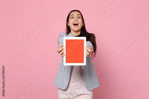 Portrait of amazed young woman in striped jacket holding tablet pc computer with blank empty screen isolated on pink pastel background. People sincere emotions, lifestyle concept. Mock up copy space.