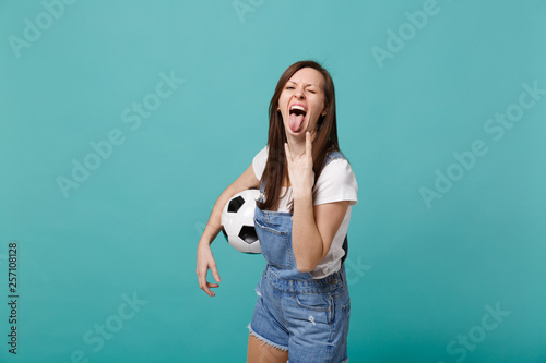 Funny woman football fan cheer up support favorite team with soccer ball showing tongue heavy metal rock sign isolated on blue turquoise wall background. People emotions, sport family leisure concept. © ViDi Studio