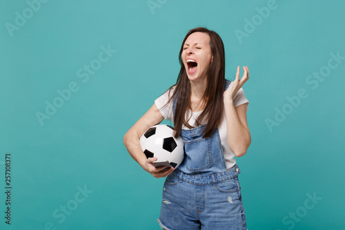 Displeased screaming woman football fan with soccer ball using mobile phone, spreading hands isolated on blue turquoise background. People emotions, sport family leisure concept. Mock up copy space. © ViDi Studio