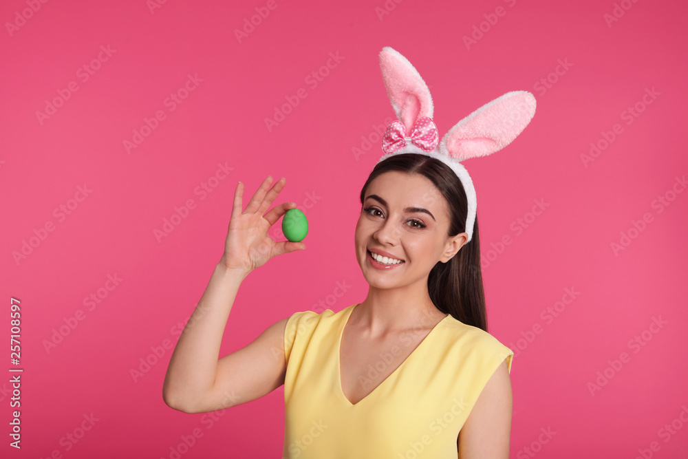 Beautiful woman in bunny ears headband holding Easter egg on color background Beautiful woman in bunny ears headband holding Easter egg on color background