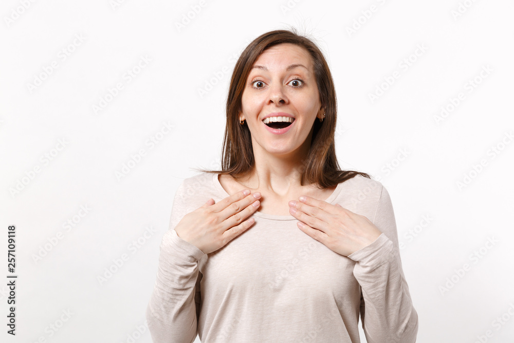Portrait of surprised excited young woman in light clothes keeping mouth open, holding hands on chest isolated on white wall background. People sincere emotions, lifestyle concept. Mock up copy space. Portrait of surprised excited young woman in light clothes keeping mouth open, holding hands on chest isolated on white wall background. People sincere emotions, lifestyle concept. Mock up copy space.