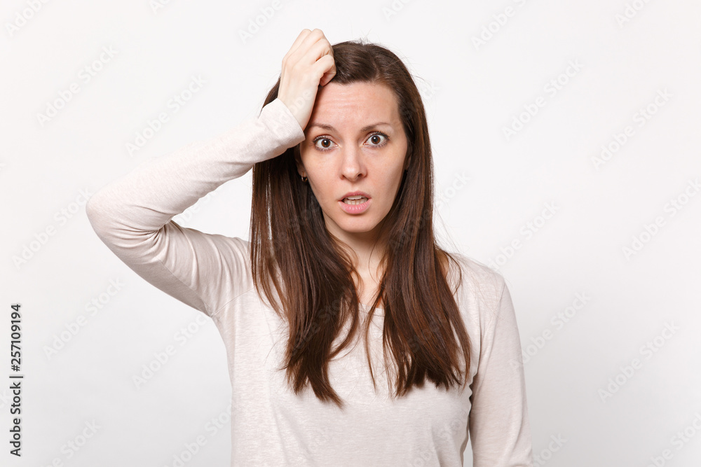 Portrait of preoccupied young woman in light clothes looking camera putting hand on head isolated on white wall background in studio. People sincere emotions, lifestyle concept. Mock up copy space.