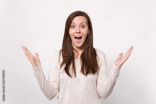 Portrait of surprised young woman in light clothes keeping mouth wide open, spreading hands isolated on white wall background in studio. People sincere emotions, lifestyle concept. Mock up copy space.