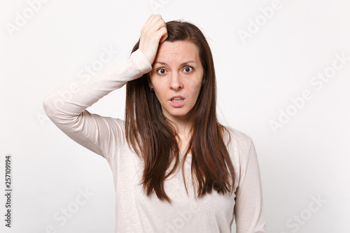 Portrait of preoccupied young woman in light clothes looking camera putting hand on head isolated on white wall background in studio. People sincere emotions, lifestyle concept. Mock up copy space.
