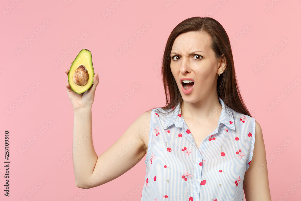 Concerned perplexed young woman in summer clothes holding half of fresh ripe green avocado fruit isolated on pink pastel background. People vivid lifestyle relax vacation concept. Mock up copy space. Concerned perplexed young woman in summer clothes holding half of fresh ripe green avocado fruit isolated on pink pastel background. People vivid lifestyle relax vacation concept. Mock up copy space.