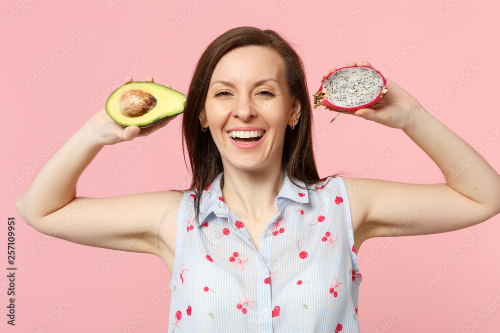 Smiling young woman in summer clothes holding fresh ripe green avocado pitahaya dragon fruit isolated on pink pastel wall background. People vivid lifestyle relax vacation concept. Mock up copy space.