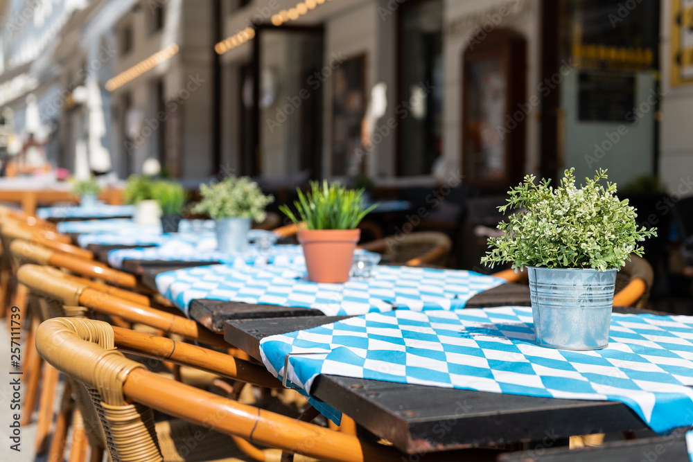 Closeup of empty blue tables outside restaurant cafe chair on sidewalk street green potted flowers plants flowerpot potted setting nobody