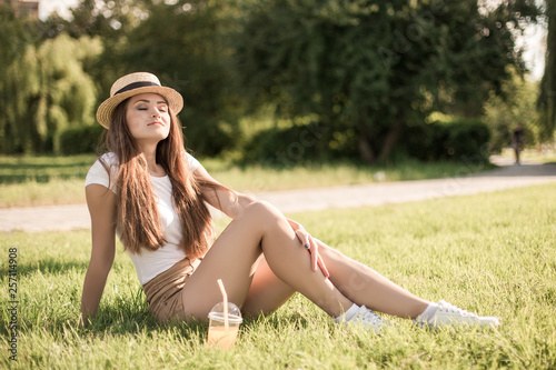 Beautiful young woman relaxing in summer park with cold orange juice. © zadorozhna