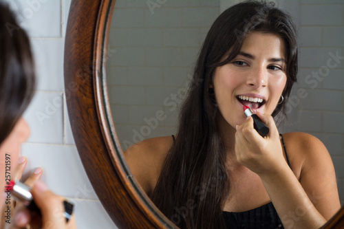 Woman applying red lipstick in bathroom.