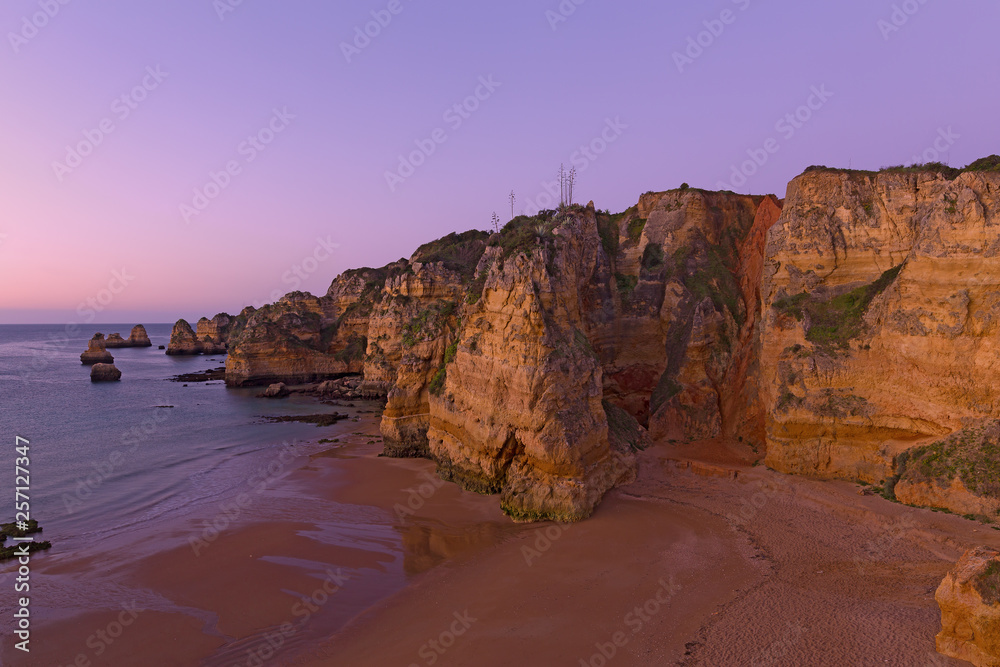 Empty sandy beach with whimsy cliffs at sunrise in Lagos, Portugal. Cloudy sunrise over the Atlantic Ocean.